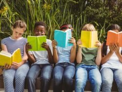 Elementary Kids sitting on a ledge in a garden setting reading books. Lots of color, boys and girls.