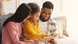 Young couple, a mom and a dad, reading with their young daughter. Montessori learning reading at home.