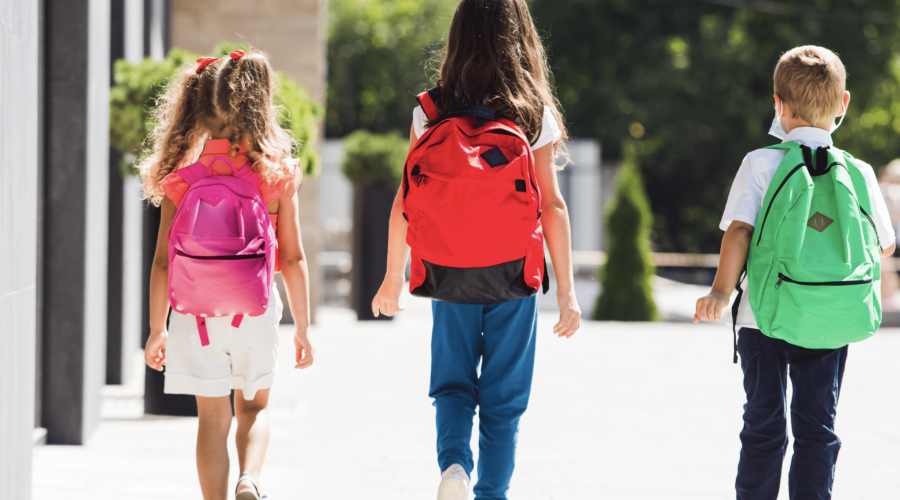 Elementary Students walking into school with back to school essentials and new backpacks