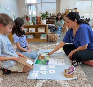 Femaie and Male Elementary Students learning the Literacy Program from teacher/guide in a Montessori Classroom , sitting on the floor of classsroom