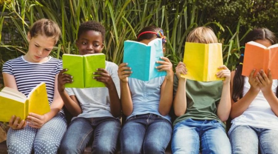 Elementary Kids sitting on a ledge in a garden setting reading books. Lots of color, boys and girls.