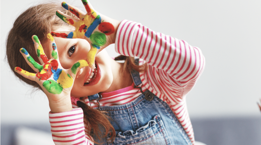 Young girl in braids in a red and white striped shirt and overalls with colorful paint on her hands from fingerpainting cherishing meaningful moments in the holiday season